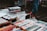 A street market table displaying paperback books for sale at £1 each. The table is filled with various books and DVDs, and a person wearing pink socks and white shoes is visible in the background.