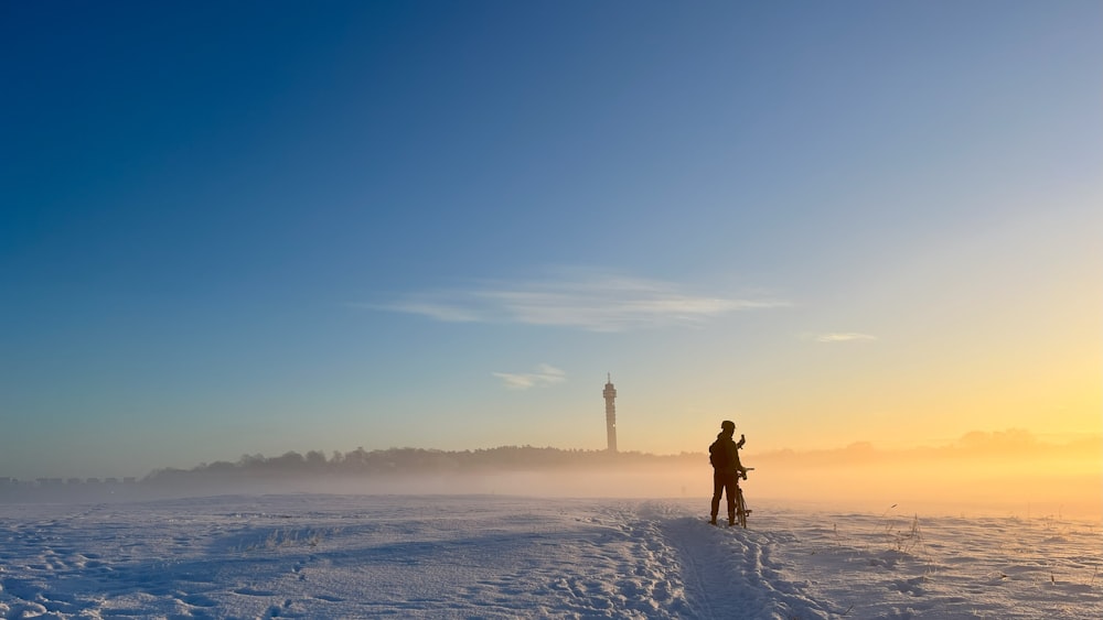 a person standing in the snow with a tower in the background