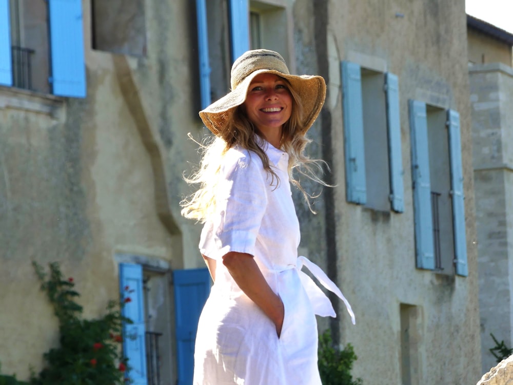 a woman in a white dress and hat standing in front of a building