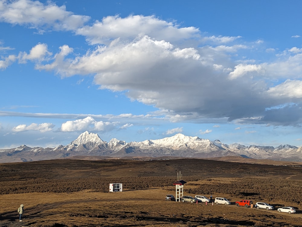 a field with a few cars parked in front of a mountain range