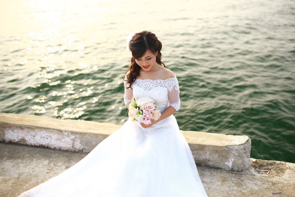 a woman in a white wedding dress standing by the water