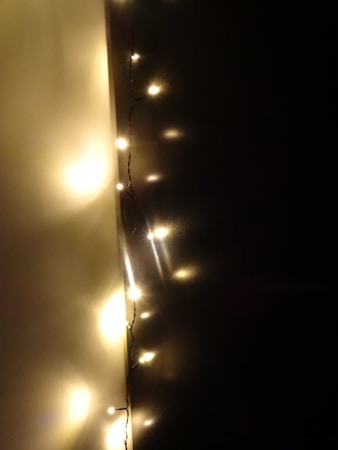 A strand of warm white fairy lights is hung against a dark wall, creating a cozy and intimate ambiance. The lights are small and emit a soft glow, casting gentle reflections on the surface around them.