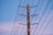 A wooden utility pole with several horizontal crossarms and connecting electrical wires set against a clear blue sky.