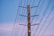 A wooden utility pole with several horizontal crossarms and connecting electrical wires set against a clear blue sky.