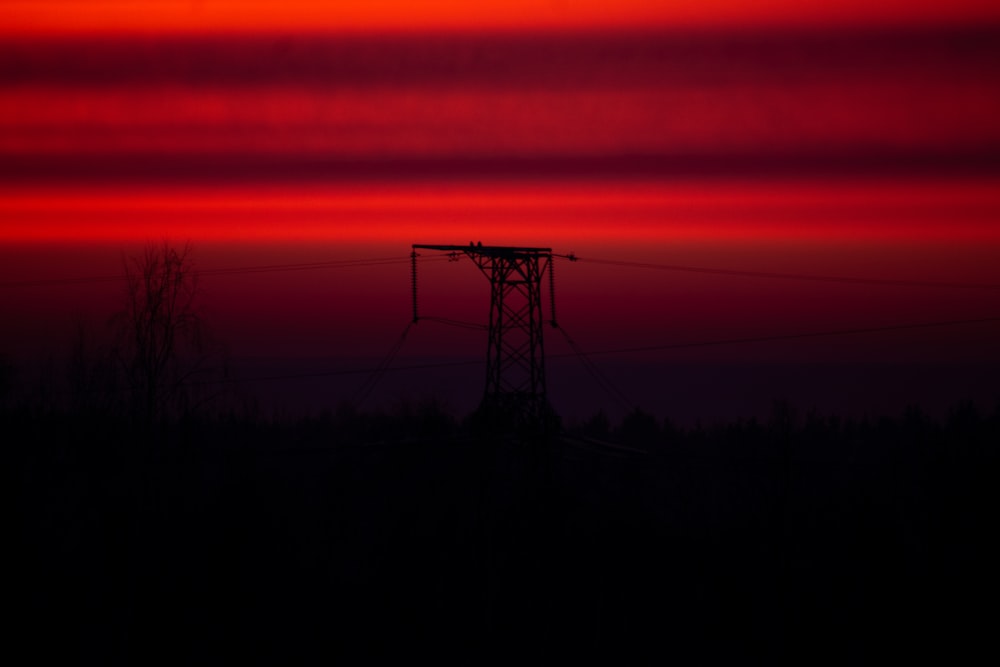 a red sky with a line of power lines in the foreground