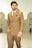 A man wearing a double-breasted brown suit with a white shirt and patterned tie stands confidently. The suit features a pocket square and a chain accessory. His watch is prominently displayed on his wrist. In the background, there is a large mosque-like structure with domes and arches.