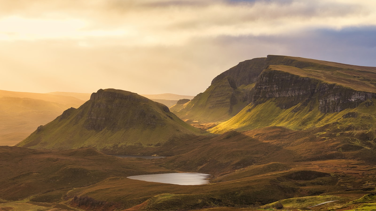 Golden light on the green cliffs and folded hills of the Quiraing with a small lochan in the valley