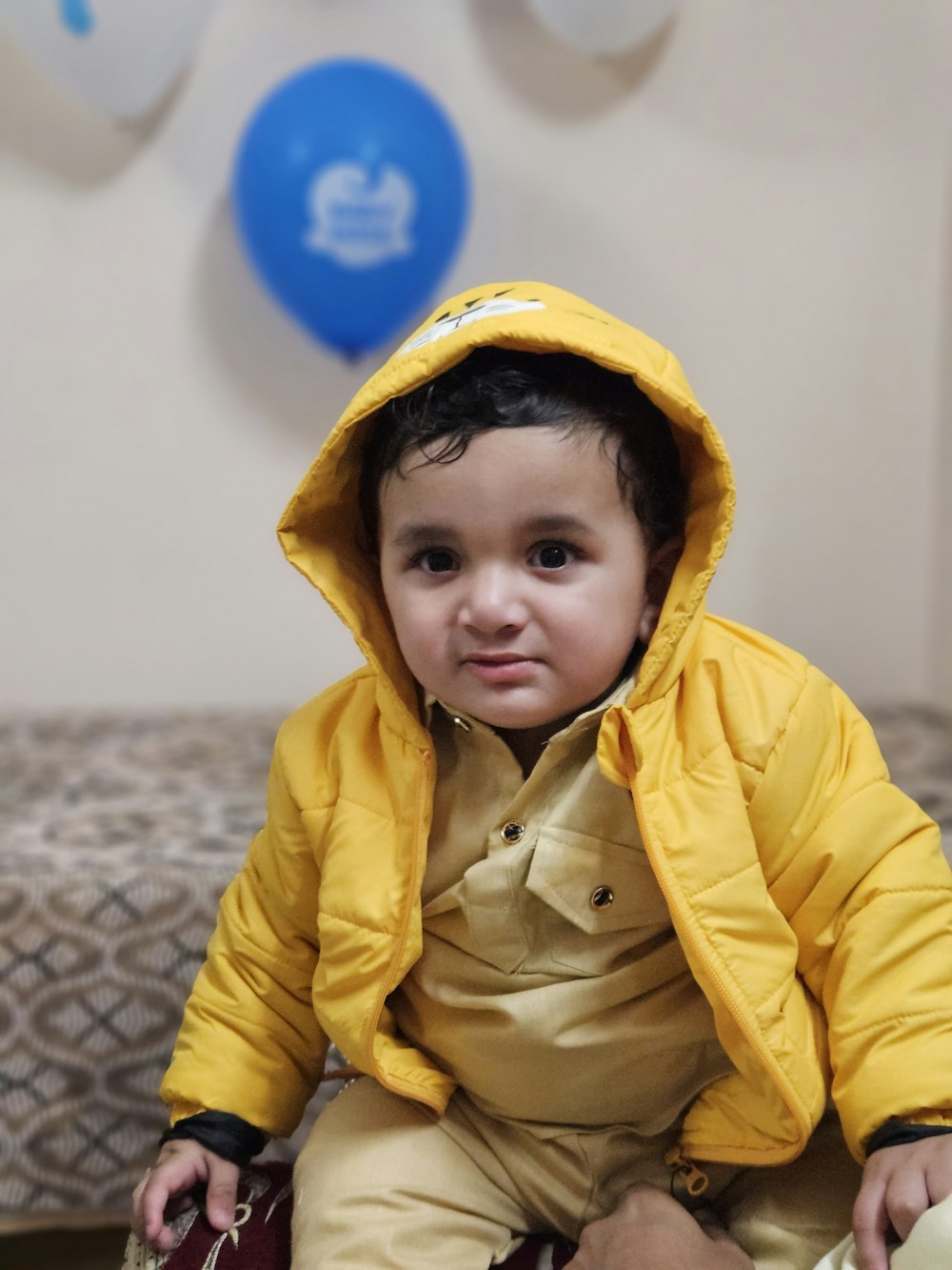 a small child in a yellow jacket sitting on a bed
