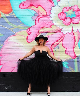 Model wearing a minimalist dress standing confidently against an urban mural.