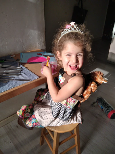 A joyful toddler proudly holding a colorful finished activity book page with crayons scattered around.
