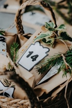 A woven basket contains brown paper bags decorated with greenery and a card displaying the number 14. The setting appears to be festive, potentially part of an Advent calendar or a holiday countdown.
