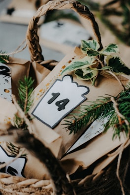 A woven basket contains brown paper bags decorated with greenery and a card displaying the number 14. The setting appears to be festive, potentially part of an Advent calendar or a holiday countdown.