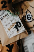 A collection of wrapped holiday gifts with decorative paper and tags featuring festive words like 'Holiday' and 'New Year.' The number 10 is prominently displayed on one of the tags, and there are pine sprigs for a natural touch. The colors include warm browns and golds, creating a cozy and festive atmosphere.