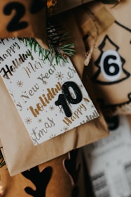 A collection of wrapped holiday gifts with decorative paper and tags featuring festive words like 'Holiday' and 'New Year.' The number 10 is prominently displayed on one of the tags, and there are pine sprigs for a natural touch. The colors include warm browns and golds, creating a cozy and festive atmosphere.