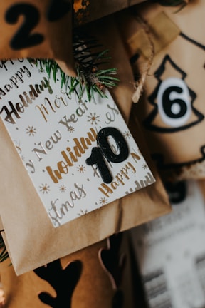 A collection of wrapped holiday gifts with decorative paper and tags featuring festive words like 'Holiday' and 'New Year.' The number 10 is prominently displayed on one of the tags, and there are pine sprigs for a natural touch. The colors include warm browns and golds, creating a cozy and festive atmosphere.