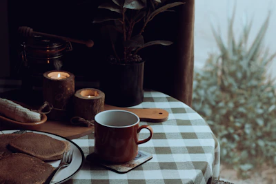 A sunlit kitchen table set with handmade ceramic mugs and plates, surrounded by fresh herbs and a soft linen tablecloth.