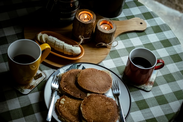 A cozy breakfast table with steaming coffee cups and plates of fluffy pancakes topped with fresh berries.