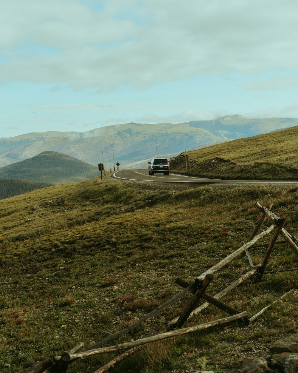 a car driving down a road next to a lush green hillside