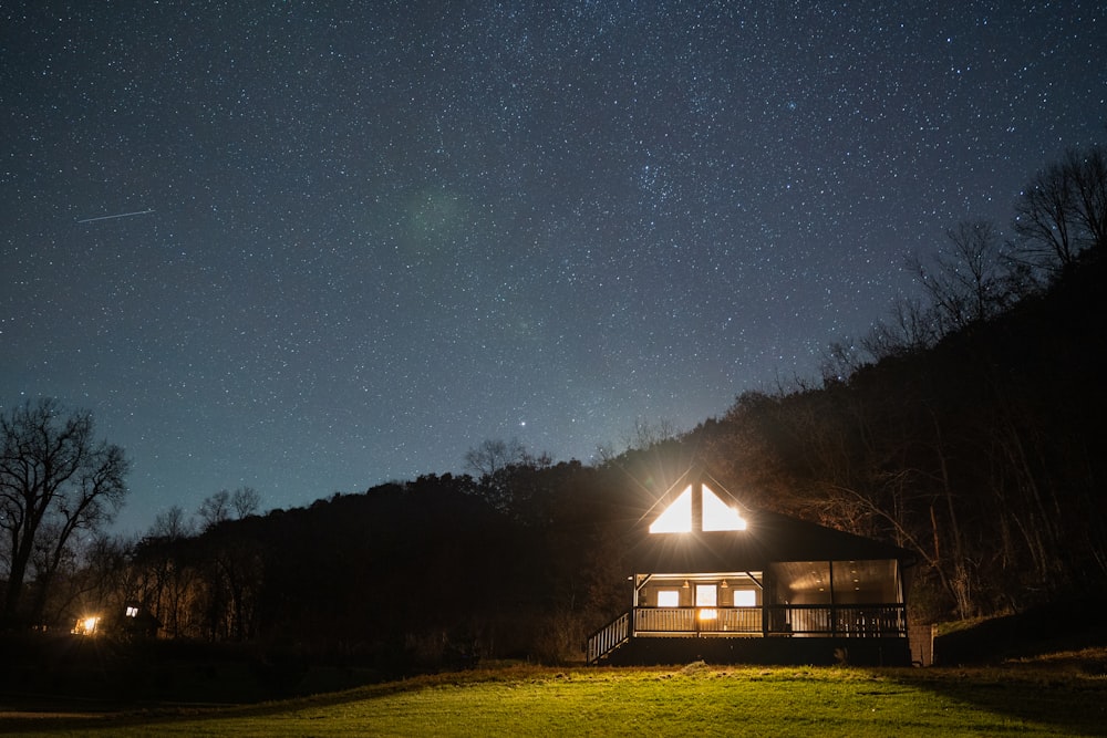 a small cabin is lit up at night under the stars