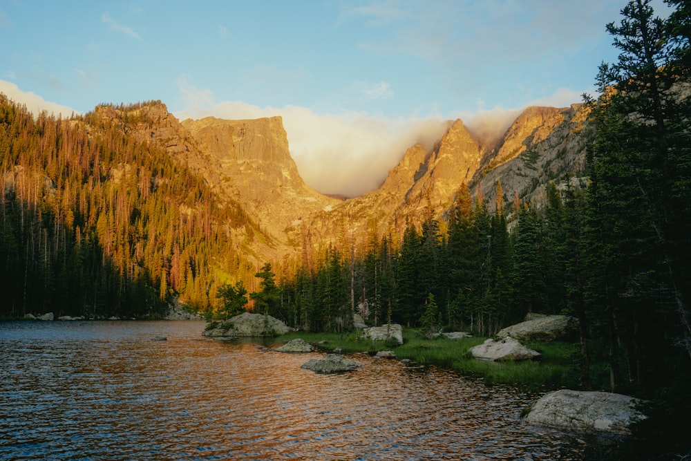 a lake surrounded by trees and mountains under a cloudy sky