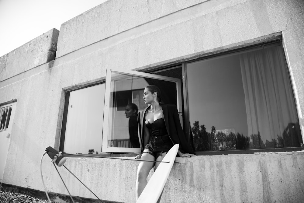 a woman sitting on a window sill holding a surfboard