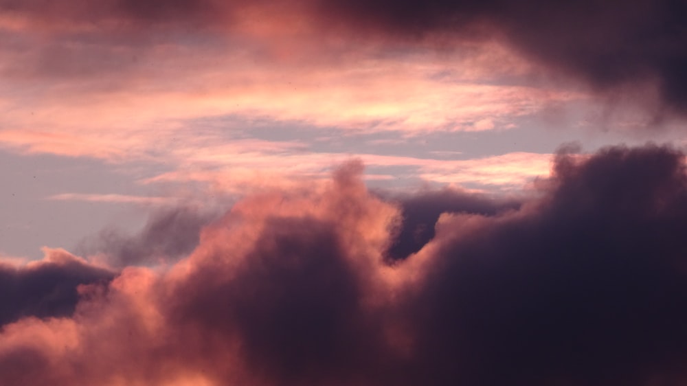 a plane flying through a cloudy sky at sunset