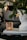 A decorative scene featuring a close-up of a Christmas tree branch with a heart-shaped cookie ornament and a star ornament. A white sculptural bust sits beside a textured amber glass candle holder on top of two magazines.