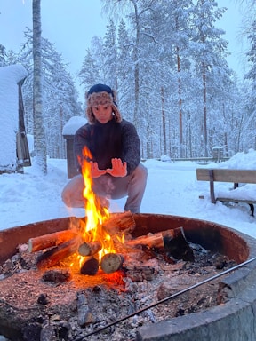 A cozy outdoor scene with rugged jackets and hats hanging on a wooden rack beside a campfire.