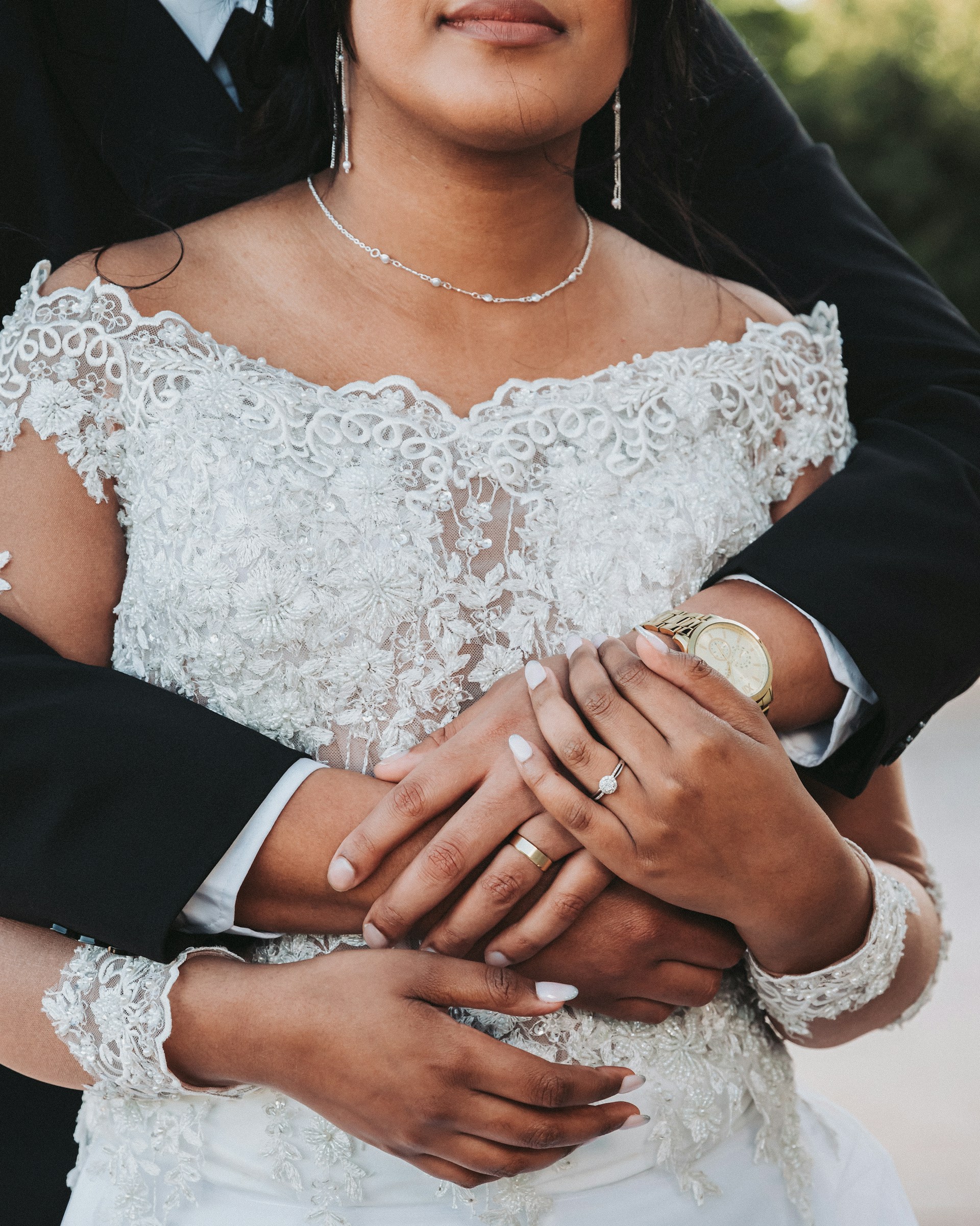 An intimate shot of intertwined hands adorned with wedding rings, set against a blurred garden background.