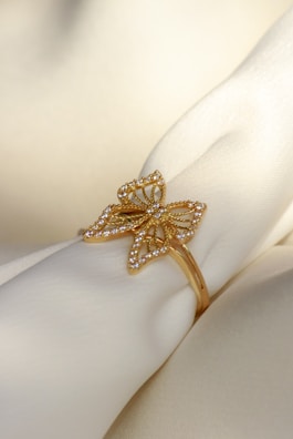 A delicate gold ring designed in the shape of a butterfly, adorned with small diamonds, resting on a soft, cream-colored fabric.