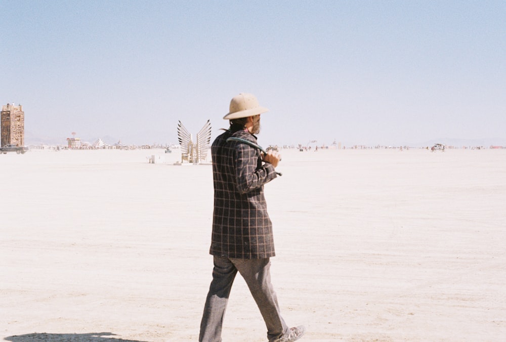 a man in a suit and hat walking across a desert