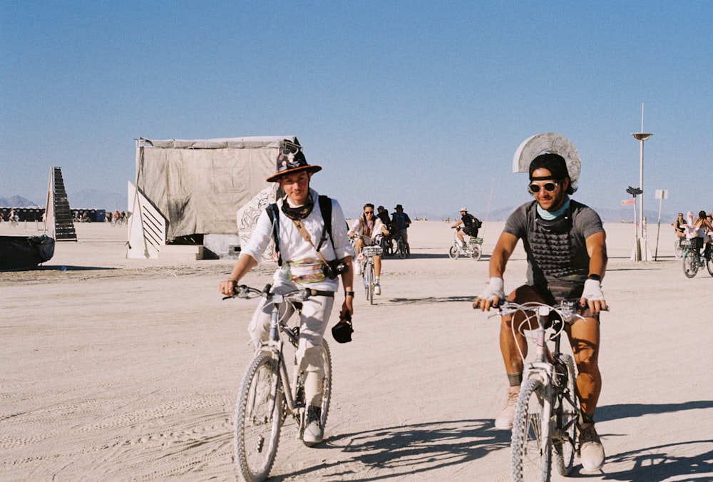 a couple of men riding bikes across a sandy field