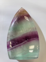 A polished, teardrop-shaped stone with a smooth surface. It features horizontal bands in shades of light purple, green, and hints of amber.