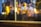 A close-up of a window display showcasing a Dior product, partially obscured by the reflection of warm, blurry lights. The scene includes hints of fashion elements such as designer clothing and a handbag, enveloped in a dreamy and artistic bokeh effect.