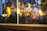 A close-up of a window display showcasing a Dior product, partially obscured by the reflection of warm, blurry lights. The scene includes hints of fashion elements such as designer clothing and a handbag, enveloped in a dreamy and artistic bokeh effect.
