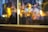 A close-up of a window display showcasing a Dior product, partially obscured by the reflection of warm, blurry lights. The scene includes hints of fashion elements such as designer clothing and a handbag, enveloped in a dreamy and artistic bokeh effect.