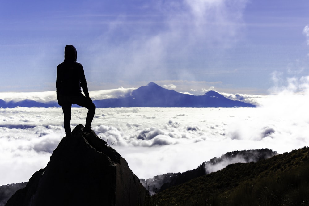 une personne assise au sommet d’une montagne au-dessus des nuages