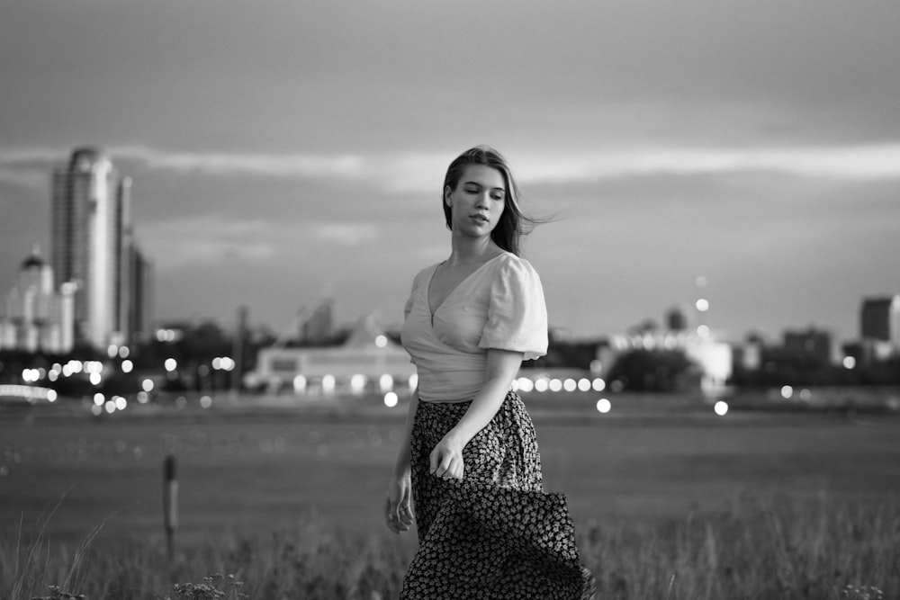 a woman standing in a field with a city in the background