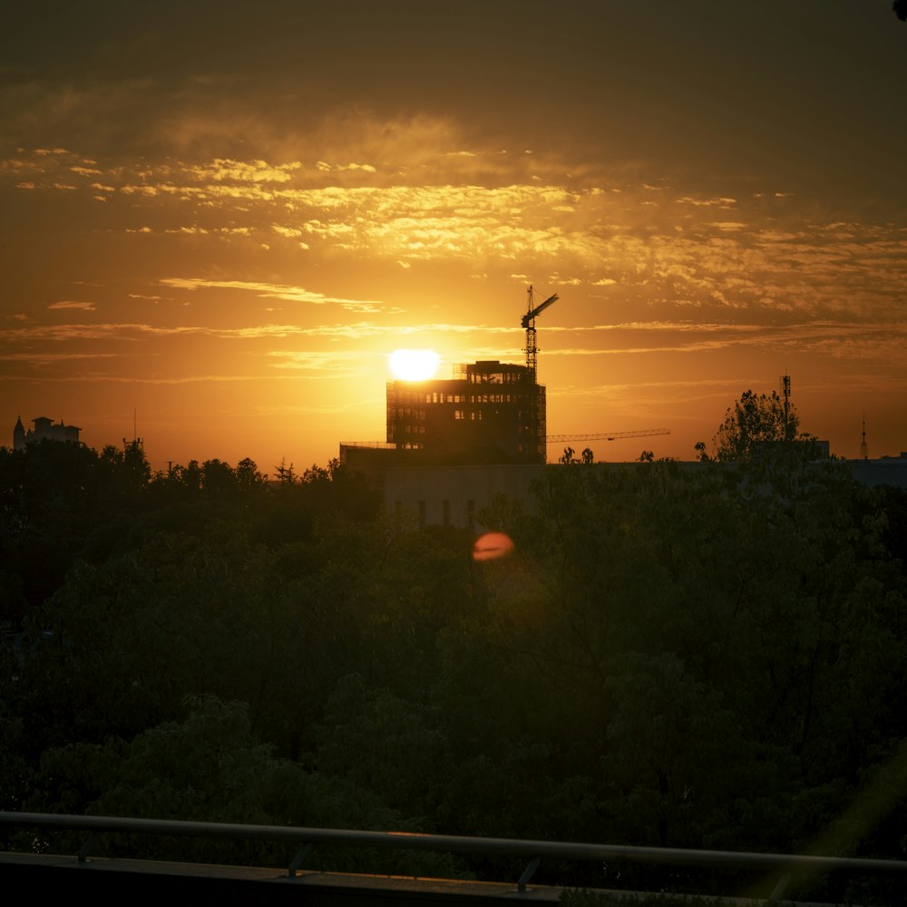 El sol se pone detrás de un edificio con una grúa en primer plano