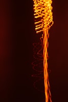 A dynamic composition featuring swirling and wavy lines of bright orange light against a deep black background, creating an impression of energy and movement.