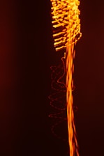 A dynamic composition featuring swirling and wavy lines of bright orange light against a deep black background, creating an impression of energy and movement.