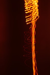 A dynamic composition featuring swirling and wavy lines of bright orange light against a deep black background, creating an impression of energy and movement.