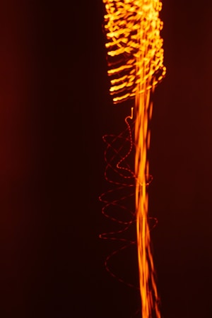 A dynamic composition featuring swirling and wavy lines of bright orange light against a deep black background, creating an impression of energy and movement.