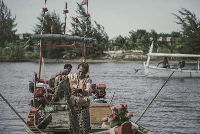 Fishermen repairing their nets on a rustic wooden boat at the edge of a river.