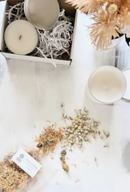 A serene arrangement of balm tins nestled among sprigs of rosemary, chamomile, and calendula flowers.