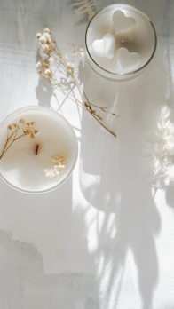 An elegant candle in a minimalist beige holder, surrounded by dried flowers and soft light.