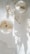 Two minimalist candles, one with small white flowers on top and another with heart-shaped wax, are placed on a light-colored surface. Delicate shadows and dried floral elements add a serene and tranquil atmosphere.