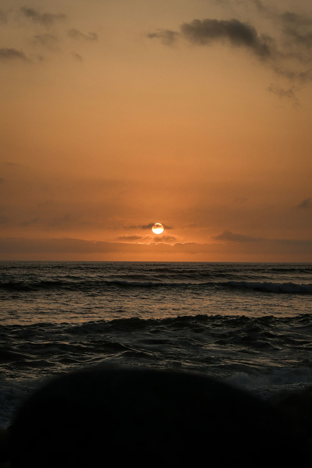 the sun is setting over the ocean on a cloudy day