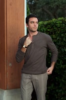 a man leaning against a wall with his hands in his pockets