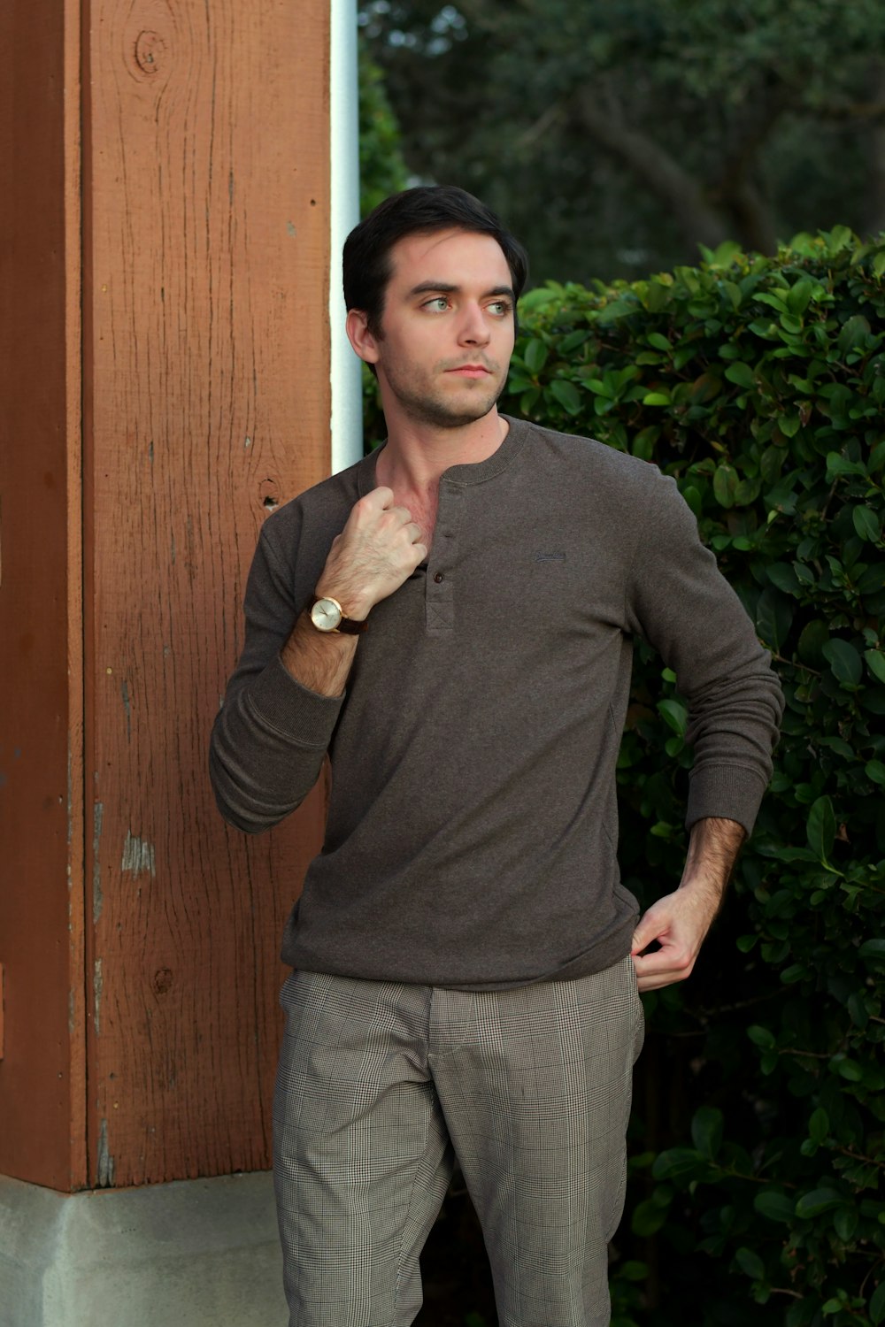 a man leaning against a wall with his hands in his pockets